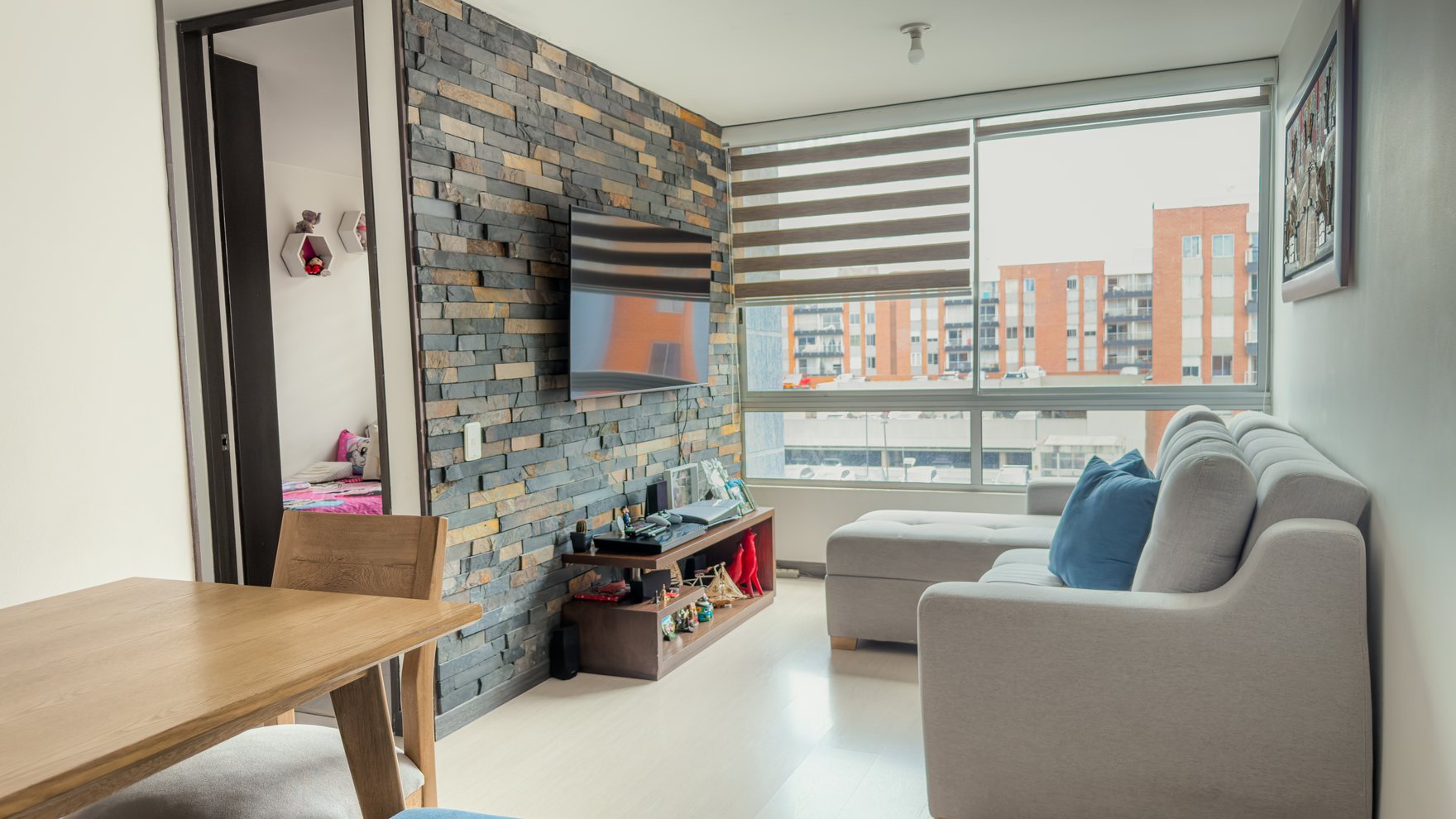 Sala comedor del apartamento del Conjunto Coruña, con muro en piedra y ventanal.
